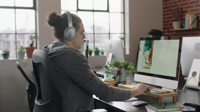 young caucasian businessman designer working on graphic design project using computer listening to music enjoying writing notes brainstorming ideas in relaxed office workplace