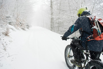 man riding with electric bicycle, e-bike, ebike, pedal on snowy road, during snow storm, blizzard,...