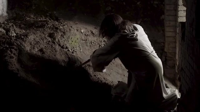 A man like Jesus Christ is digging a hole in the dungeon, a man is searching for a precious treasure, a man in a white robe is digging the earth with a stick and finds gold, Jesus hides the holy grail