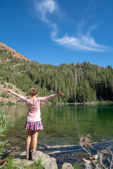 Beautiful young woman enjoying the view at Heart Lake in Mammoth Lakes California on a sunny day. Back facing camera, arms raised in joy