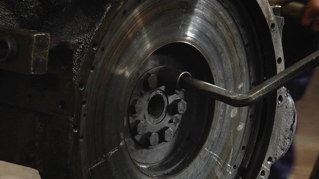 Car engine flywheel. The mechanic unscrews the key flywheel. In the workshop remove the flywheel from the car engine.