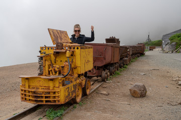 Fototapeta na wymiar Woman poses as a train conductor on a mining cart at Independence Mine Alaska at Hatcher Pass on a misty foggy day