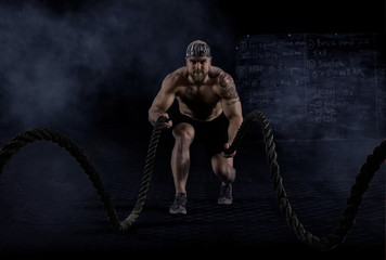 Fototapeta na wymiar Muscular man working out with battle ropes