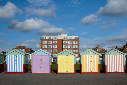 a line of five beach huts on Brighton promenade 5 beach huts are green and blue and one is multi coloured stripey yellow, pink, colours, standing out from the rest