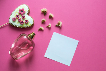 Love concept - pink adorable perfume, gingerbread heart, flowers on pink background. Copy space for text.