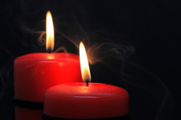 Two red candles with fire and smoke on black background.