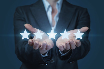 A businesswoman is holding a line of golden shining stars at the dark background.