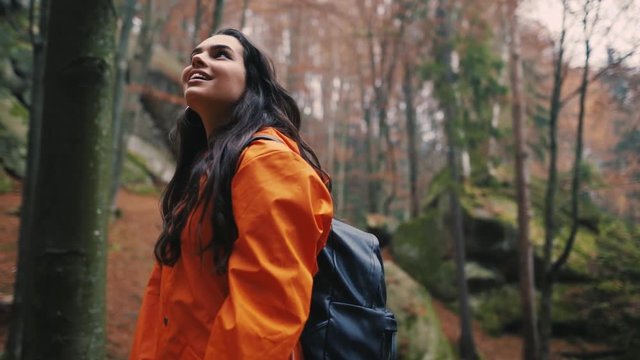 Charming brunette attractive young woman stand smile look around in forest outdoors with yellow leaves foliage autumn backpack hiker vacation portrait slow motion