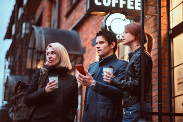 Fototapeta premium Three friends students having a break with coffee near a cafe outside.