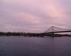 View across the river to the bridge in the distance and the forest in the winter evening.