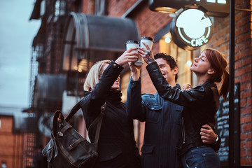 Fototapeta na wymiar Cheerful friends making a toast with coffee near a cafe outside.