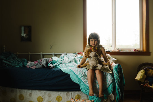 Young girl sitting on her bed with her toys on her lap