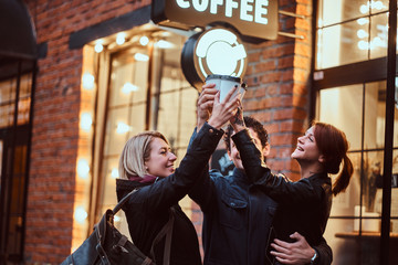 Cheerful friends making a toast with coffee near a cafe outside.
