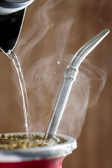 vertical close-up of hot water served into steaming yerba mate infusion