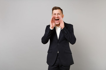 Portrait of cheerful young business man in classic black suit, shirt screaming with hand gesture isolated on grey background in studio. Achievement career wealth business concept. Mock up copy space.