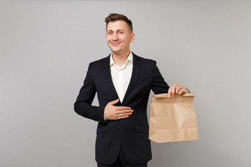 Joyful business man holding brown clear empty blank craft paper bag for takeaway mock up isolated on grey background. Achievement career wealth business concept. Food products delivery to work office.