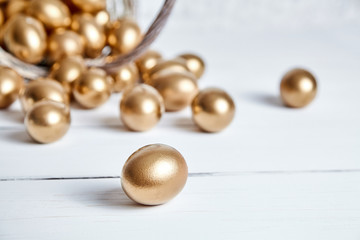 Easter golden eggs spilled out of wicker basket on white wooden table. Selective focus