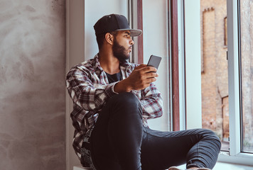 African-American bearded man sitting on a window sill.