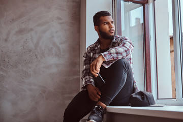 African-American bearded man sitting on a window sill.