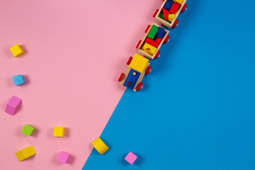 Toy background. Wooden toy train with colorful cubes on pink and blue background