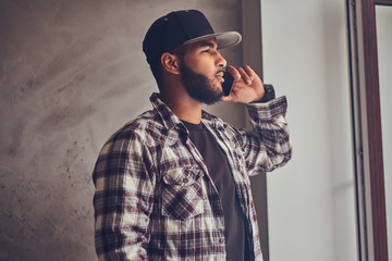 African-American bearded man wearing a checkered shirt and cap talking by phone