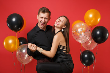 Stunning young couple in black clothes celebrating birthday holiday party isolated on bright red background air balloons. St. Valentine's International Women's Day Happy New Year 2019 concept. Mock up