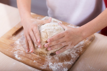 Children's hands knead the dough on a wooden cutting board. close-up. dough recipe, cooking technology