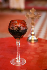 Isolated glass of vine in front and blurred wedding ceremony cross in background . Orthodox church wedding accessories