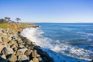 Waves crashing on the rocky shoreline of the Pacific Coast; Santa Cruz surfing museum in the...
