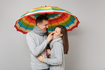 Couple girl guy in gray sweaters scarves together under umbrella isolated on grey wall background,...