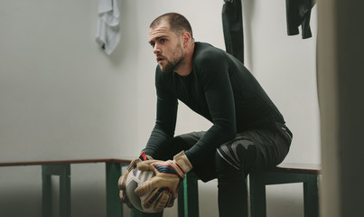 Footballer sitting in dressing room holding a football