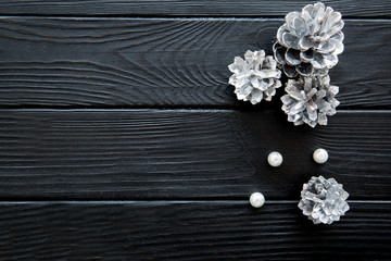 Obraz premium Silver pine cones and a heap of white beads on black wooden table. Free space for text.