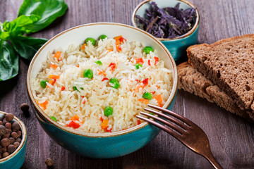 Rice with vegetables, peas, carrots, peppers on plate on wooden background. Healthy food. Top view
