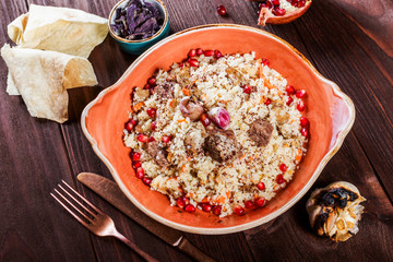 Pilaf with lamb meat, carrots, onions, garlic, pomegranate on plate on wooden background. Traditional dish of Asian cuisine. Top view