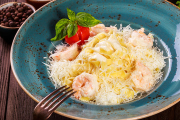 Pasta with shrimp, cheese parmesan, tomatoes, basil and cream sauce on dark wooden background, Italian cuisine. Ingredients on table. Top view