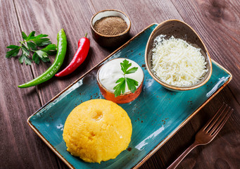 Delicious polenta - Corn porridge hominy with goat cheese, butter and sour cream on wooden background. Healthy food. Top view
