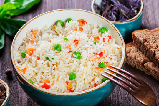 Rice with vegetables, peas, carrots, peppers on plate on wooden background. Healthy food. Top view