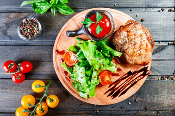 Grilled steak pork with fresh vegetable salad, tomatoes and sauce on wooden cutting board. Hot Meat Dishes. Top view