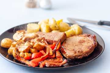 A meal of steak, potatoes, mushrooms and roasted vegetables on a black plate