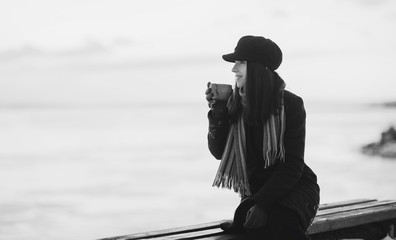 A girl in the winter on the street drinking hot coffee from a cup. How to warm up in winter or autumn and overcome depression. Black and white photo.