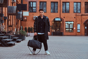 A young man trendy dressed posing and looking at camera on the street.