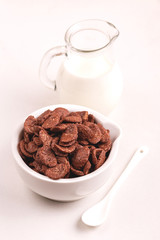 Crunchy chocolate corn flakes in bowl with jar of milk