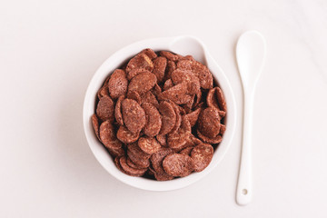 Crunchy chocolate corn flakes in bowl on light marble background