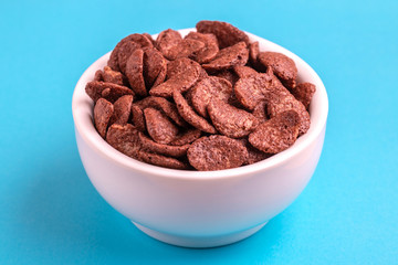 Crunchy chocolate corn flakes in bowl on bright blue background