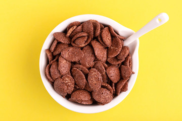 Crunchy chocolate corn flakes in bowl on bright yellow background