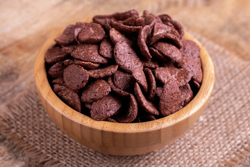 Crunchy chocolate corn flakes in wooden bowl with burlap napkin