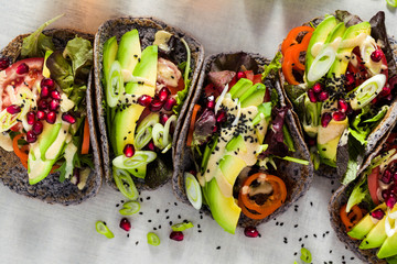 Gluten-free vegan tacos from black bean  with tomato and avocado salad  with tahini sauce and pomegranate seeds. healthy fast food for the whole family or party