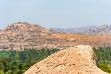 Close-up view of a granite rock with a green valley on background, Hampi, Karnataka, India.
