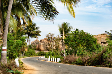 A beautiful narrow road surrounded by lush plants and granite mountains in Hampi, Karnataka, India.