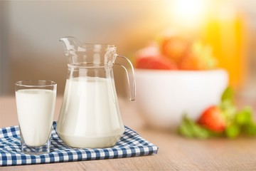 A glass of milk and a milk jug on plaid tablecloth